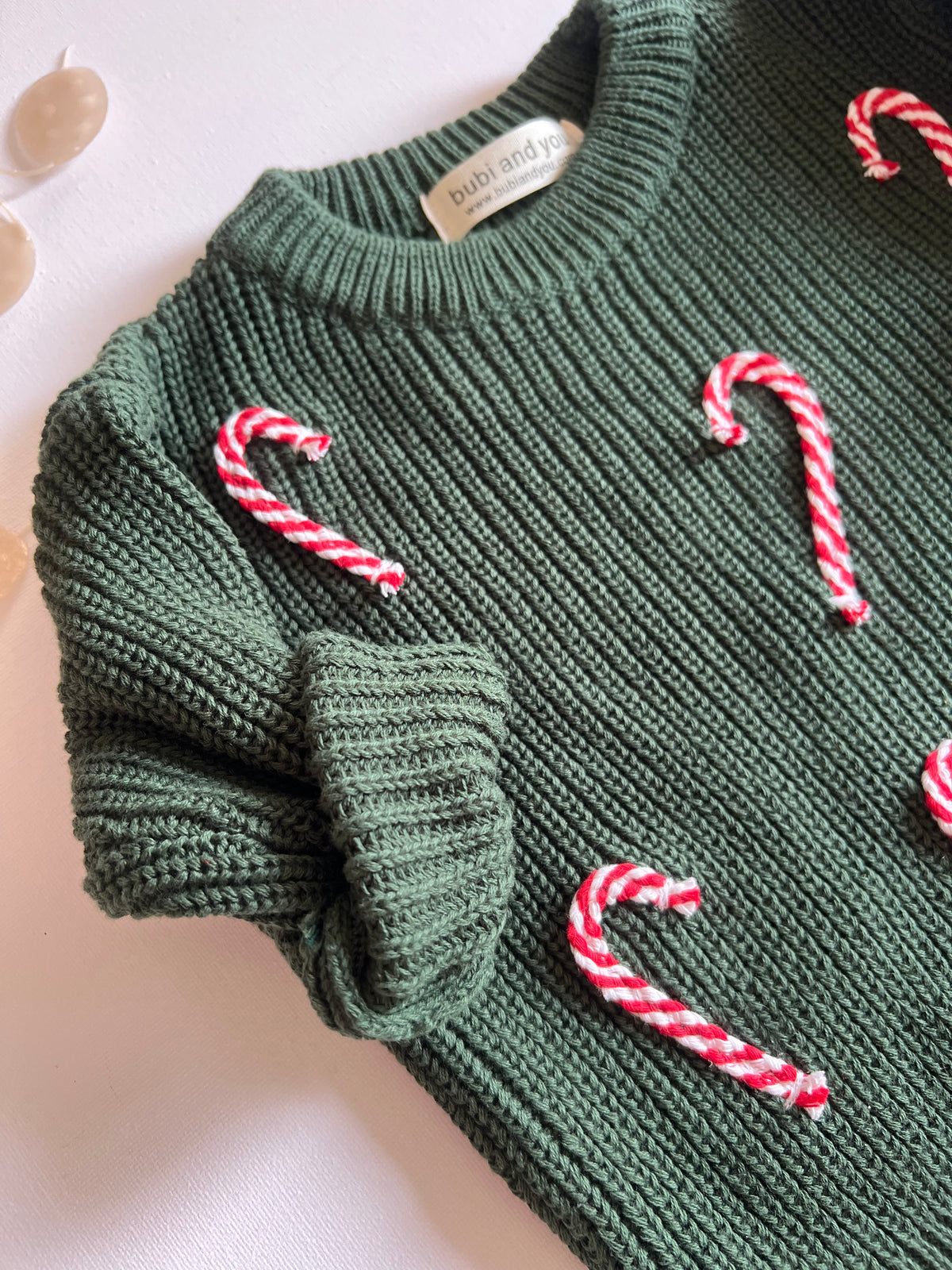 Detailansicht smaragdgrüner Weihnachtspullover mit Zuckerstangen-Applikationen
